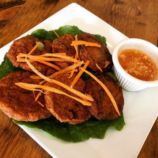 Thai fish cakes with shredded carrots on lettuce, served with a side of dipping sauce.