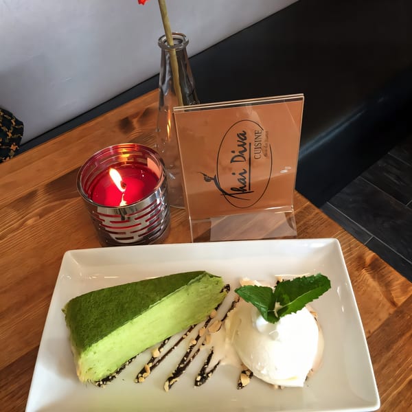 A slice of green matcha crepe cake with ice cream and a Thai Diva Cuisine menu on a wooden table.