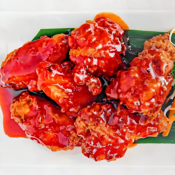 Crispy Thai Diva Cuisine chicken wings coated in a vibrant red sweet chili sauce, garnished with carrots.