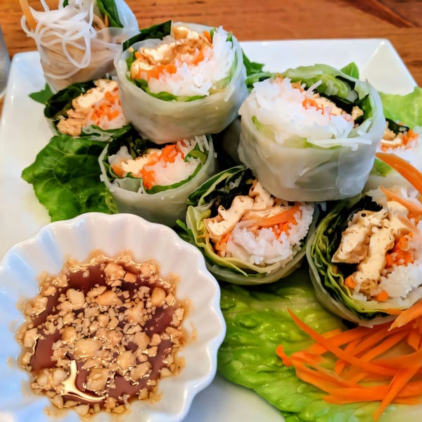 Fresh Thai spring rolls with tofu, rice noodles, and carrots, served with peanut dipping sauce.