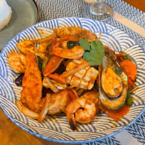 A Thai seafood dish with shrimp, squid, mussels, and vegetables in a rich orange sauce.