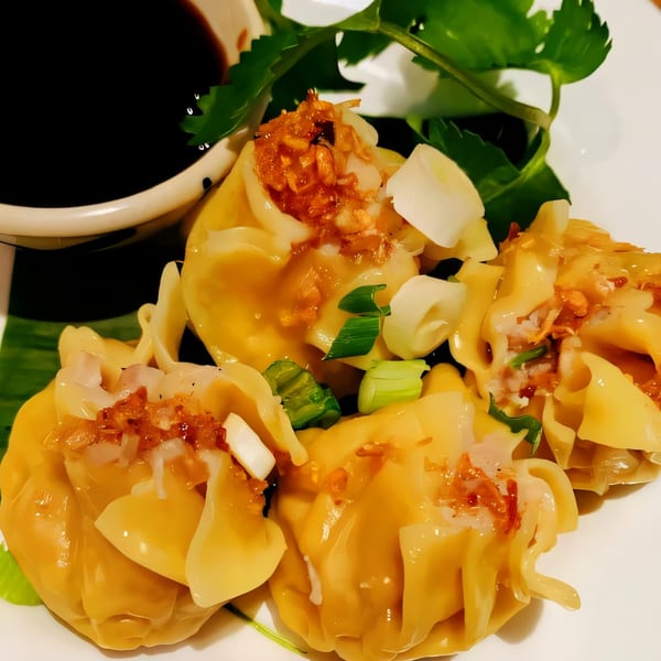 Close-up of Thai Diva Cuisine's steamed dumplings, garnished with fried garlic, green onions, and a side of soy sauce.